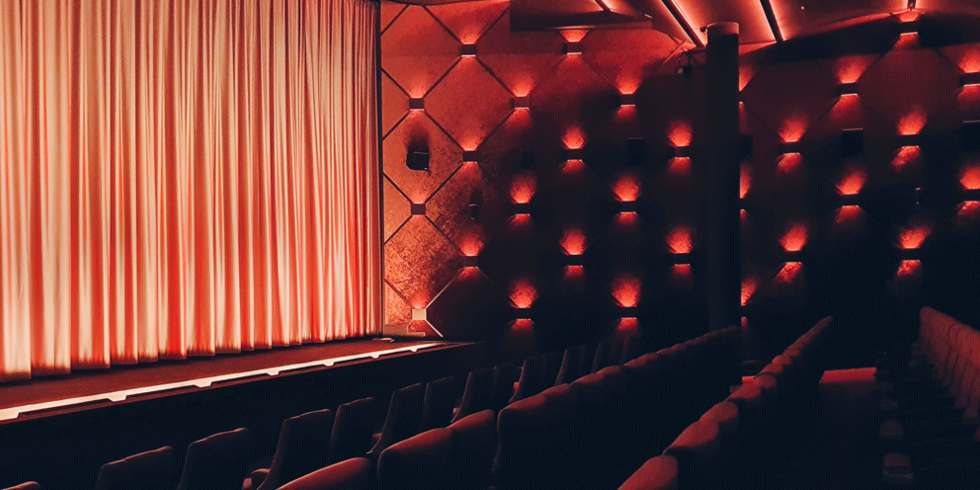 Kinosaal mit Sitzen und Bühne mit roten Lichtern beleuchtet.