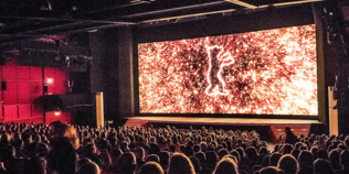 Berlinale-Bär auf einer Kinoleinwand vor einem sitzenden Publikum.