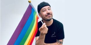 Profilbild von Stuart Bruce Cameron mit Regenbogenfahne vor grauer Wand