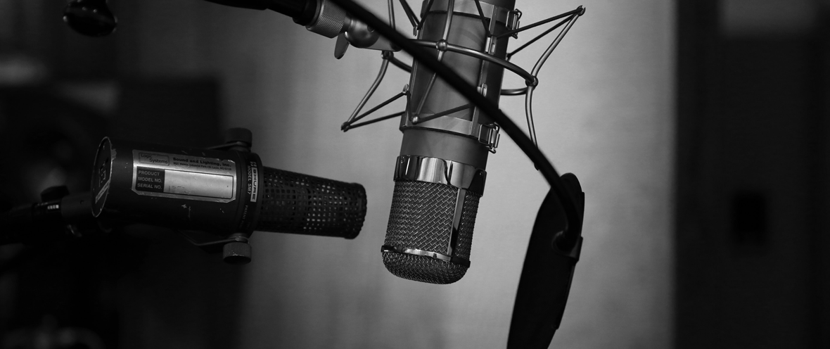 Black and white image of microphone in a recording studio in front of a grey wall.