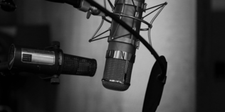 Schwarz-Weiß-Bild von Mikrofon im Aufnahmestudio vor einer grauen Wand.